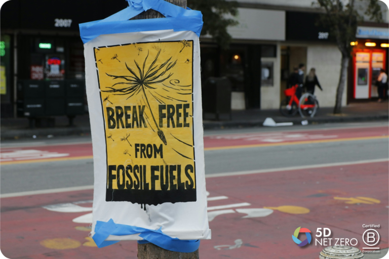 A yellow poster taped to a pole reads "BREAK FREE FROM FOSSIL FUELS" with a dandelion illustration, hinting at the importance of ESG and carbon accounting. The background shows a street, pavement, buildings, and people walking or with bicycles.