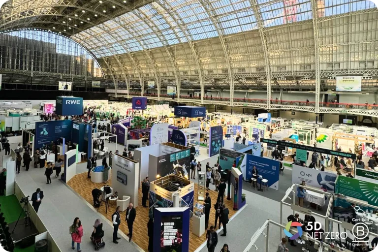 A large exhibition hall filled with numerous stands, display units, and attendees walking around at a trade show or conference.